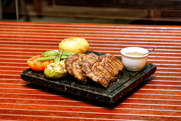 grilled pork ribs with vegetables and sauce on a wooden board