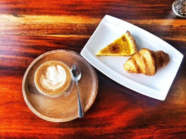 Middag koffie pauze in een café - hete latte met croissant en passievrucht tarte — Stockfoto