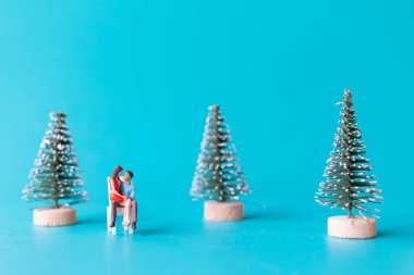Minyatür insanlar, birbirine aşık bir çift Noel ağacının yanında oturuyor, Noel ve mutlu yıllar konsepti..