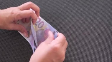 Siyah arka planda 20 Euro 'luk banknotları sayan kadın.