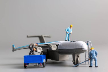 Minyatür işçi takımı gri arka planda uçakları kontrol edip onarıyor.