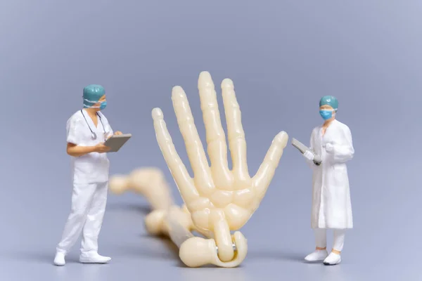 Miniaturmenschen Doktor Mit Einem Riesigen Menschlichen Knochen Auf Grauem Hintergrund — Stockfoto
