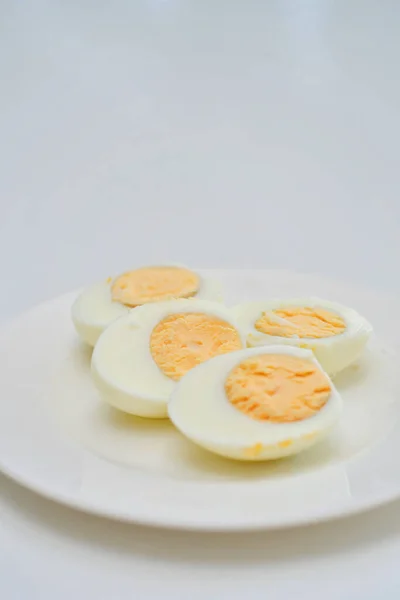 キッチンテーブルにゆで卵 健康的な朝食とタンパク質豊富な食事 脇にナイフで皿の上の卵 緑の植物とテーブルからの光の反射と風通しの良い白の背景 — ストック写真