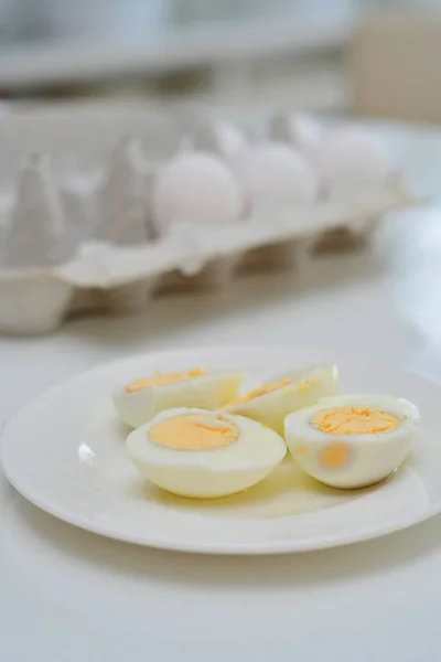 煮鸡蛋放在厨房桌子上 健康的早餐和蛋白质丰富的饮食 鸡蛋放在盘子里 旁边有一把刀 背景是通风的 白色的 绿色的植物 桌上有光的倒影 — 图库照片