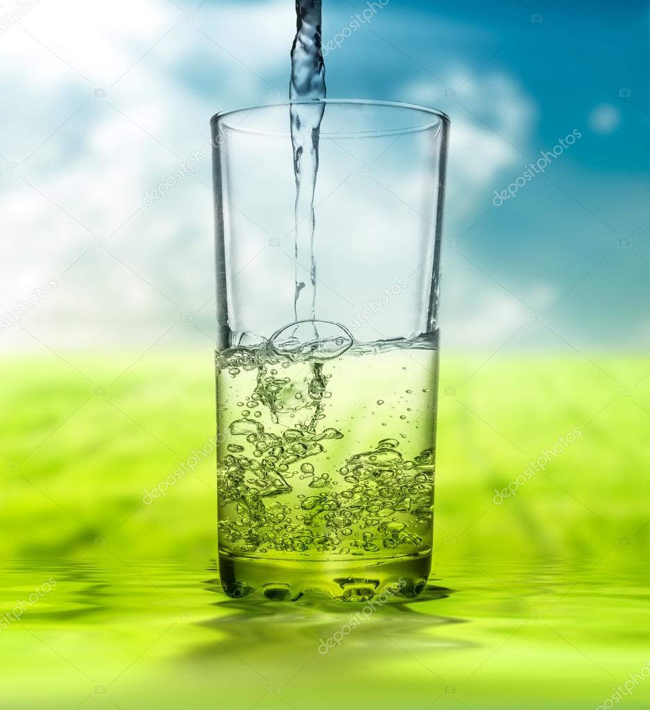 Water pouring into glass on  unfocused nature background