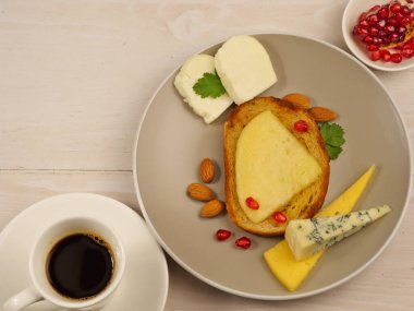 Peynirli sandviç, gri tabakta dilimlenmiş peynir. Bir fincan kahve, nar tohumu, badem, Dor Blue peyniri, Suluguni. Üst Manzara. Atıştırmalık, kahve molası, hızlı kahvaltı. Yakın plan. Düzgün beslenme. Metin için boşluk.