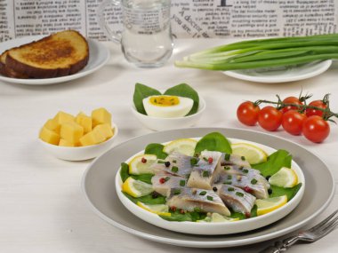 Beyaz arka planda ıspanak yapraklı limonlu tuzlu ringa fileto. Kirazlı domates, peynir, yumurta, yeşil soğan, kızarmış ekmek, bir bardak su. Aperatif. Kahvaltıda. Rus mutfağı..