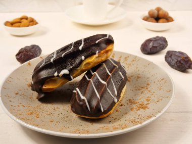 Chocolate cakes with custard and chocolate glaze. Almonds, dates on a white background. A cup of coffee. Close-up. Selective focus.