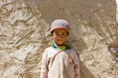 Zanskar, Hindistan - Temmuz 2012: Ladakh 'ın Zanskar kentindeki Himalaya köyünde eski bir evin kırsal çamurlu duvarının önünde yün bir kafatası takmış genç bir kızın portresi.