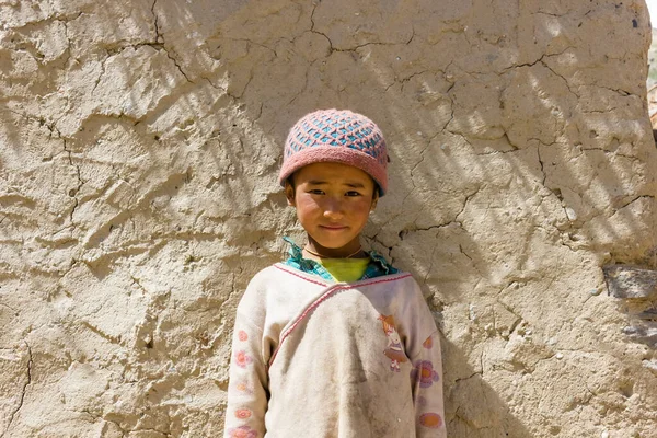 Zanskar, Hindistan - Temmuz 2012: Ladakh 'ın Zanskar kentindeki Himalaya köyünde eski bir evin kırsal çamurlu duvarının önünde yün bir kafatası takmış genç bir kızın portresi.
