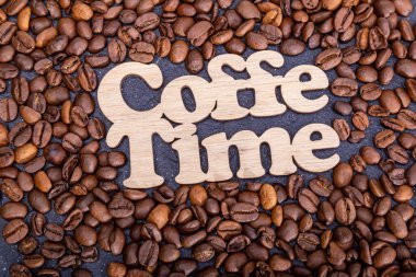 Texture background of coffee beans for design with the inscription coffee time. Coffee grains scattered on the table.