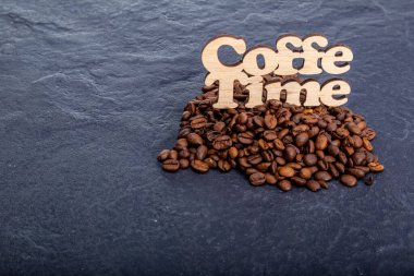 Texture background of coffee beans for design with the inscription coffee time. Coffee grains scattered on the table.