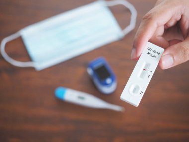İnsan eli ATK ya da antijen test kiti ahşap masada Covid-19 Coronavirus 'un korunması için pozitif ve kendine özgü testler gösteriyor..