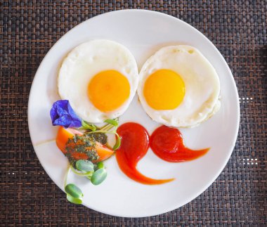 Domates soslu iki sahanda yumurta ve örülmüş bambu kaplamalı beyaz tabakta sebze..