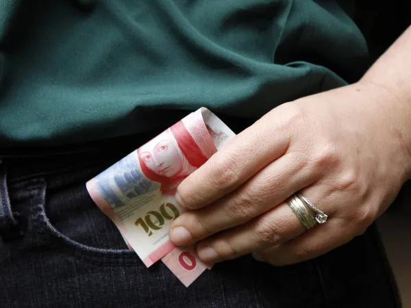 Meksika parasını kot pantolonun cebine koyan bir kadının eli.