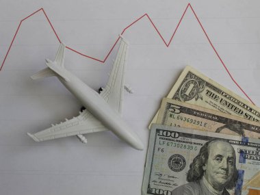 Amerikan banknotları ve beyaz bir uçağın aşağı doğru eğilimli grafiği.