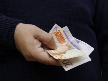 Elinde farklı değerlerde İsveç banknotları tutan bir adamın eli.