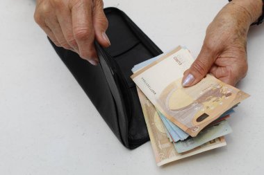 Avrupa banknotları ve siyah deri cüzdan tutan yaşlı bir kadının elleri