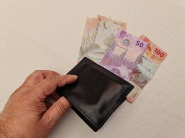 Elinde deri bir cüzdan ve Meksika banknotları var.