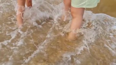 Sahilde iki kadının ayaklarını kaplayan deniz dalgası, yavaş çekim videosu.