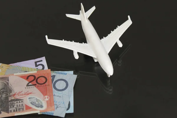 stacked australian banknotes and figure of a white plane on a glass table with reflection