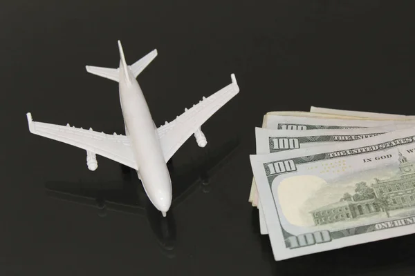 stacked american banknotes and figure of a white plane on a glass table with reflection