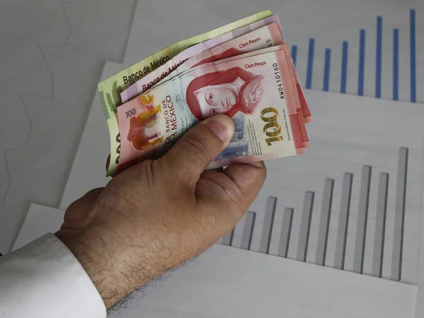 hand of a man with mexican banknotes and upward trend graphs
