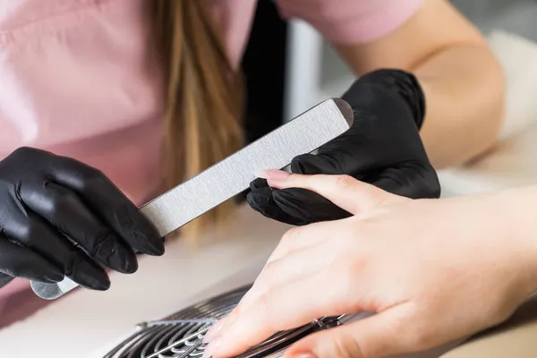 Een manicure vijlt nagels met een metalen dossier. Manicure proces in een schoonheidssalon. — Stockfoto