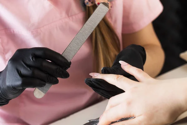 Een manicure vijlt nagels met een metalen dossier. Manicure proces in een schoonheidssalon. — Stockfoto