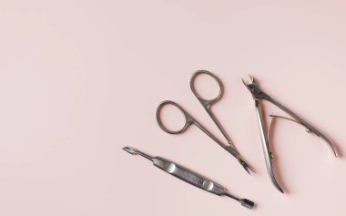 Açık pembe yüzey üzerinde kırpıcı makas seti ve tırnak itici manikür araçları
