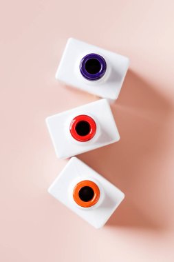 Renkli cila şişeleri, çivi kabukları açık pembe arka planda duruyor.