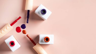 Açık pembe arka planda parlak tırnak cilası şişelerinin farklı renk fırçaları. Boşluğu kopyala.