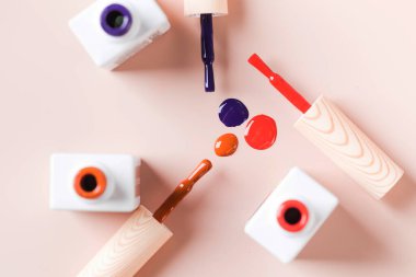 Açık pembe arka planda parlak tırnak cilası şişelerinin farklı renk fırçaları. 