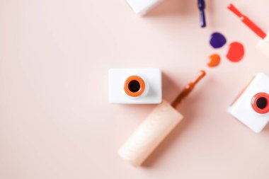 Açık pembe arka planda parlak tırnak cilası şişelerinin farklı renk fırçaları. 