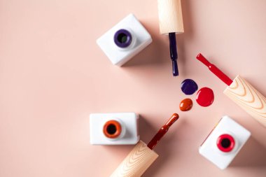 Açık pembe arka planda parlak tırnak cilası şişelerinin farklı renk fırçaları. Boşluğu kopyala.