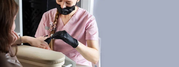 Una manicurista limpia las uñas con una lima metálica. Proceso de manicura en un salón de belleza. Banner. Copiar espacio — Foto de Stock