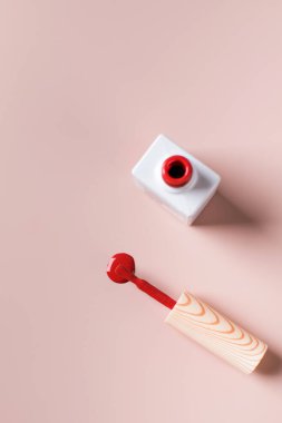 Açık kırmızı oje şişesi, fırça ve pembe arka planda bir parça oje. Boşluğu kopyala..