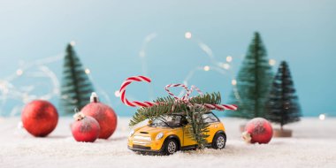 Köknar dalı, şeker kamışı ve karda küçük Noel ağaçları olan oyuncak araba.