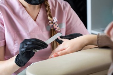  Bir manikürcü metal bir dosyayla çivi çakıyor. Güzellik salonunda manikür işlemi.