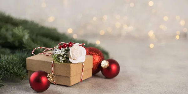 Kerstgeschenkdoos op een achtergrond van kerstboomtakken, rode kerstballen en kerstverlichting. Kopieerruimte. — Stockfoto