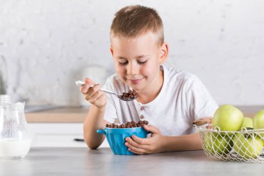 Mutlu çocuk sağlıklı kuru kahvaltı yapar. Mutfaktaki masada süt ile oturur.