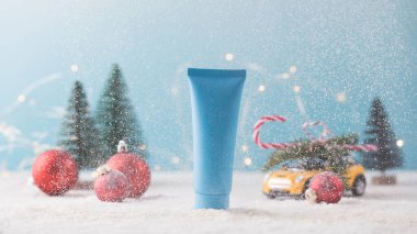 Kar yağan bir Noel arka planında kozmetik ürünü olan mavi bir tüp. Yeni yıl hediyesi..