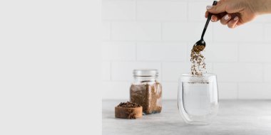 Kadın hazır kahveyi gri taş masadaki sıcak su bardağına doldurur.