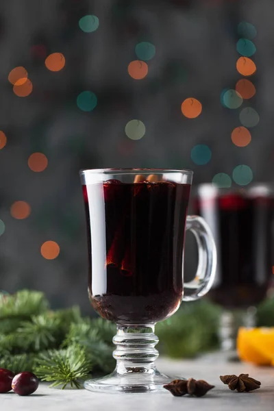 Copos com vinho caseiro mulled em um fundo de Natal com ramos de uma árvore de Natal, cranberries e bokeh. — Fotografia de Stock