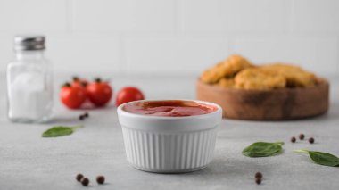  Beyaz bir kasede ketçap domateslerin arka planına karşı ve hafif bir mutfakta bir kase nugget..