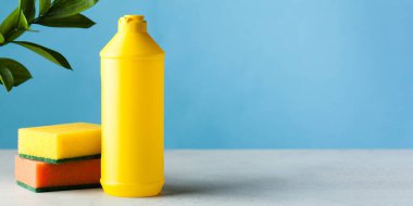 Mavi arka planda bulaşık jeli ve süngerli sarı bir şişe..