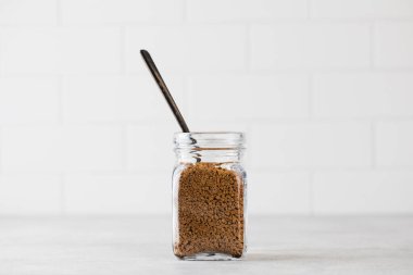 Hafif arka planda kaşıkla hazır kahvenin olduğu cam kavanoz. Boşluğu kopyala.