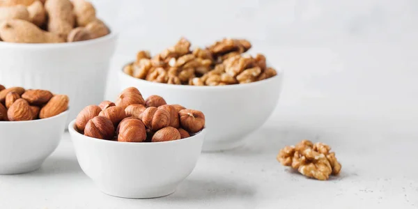 Hazelnuts and other nuts in white bowls on a white background. Banner — Stock fotografie