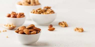Almonds and other nuts in white bowls on a white background. Banner
