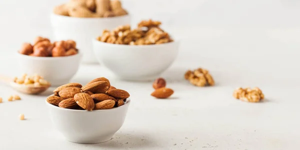 Almonds and other nuts in white bowls on a white background. Banner — Stock fotografie